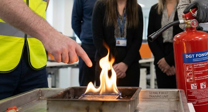 Close-up macro view of a fire extinguisher nozzle and controlled training flame during a workplace fire safety demonstration.